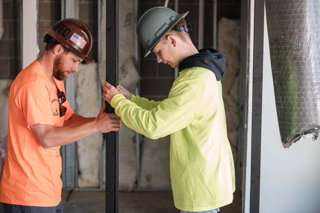 Two McIntyre Glass installers fitting a storefront glass panel on a commercial building